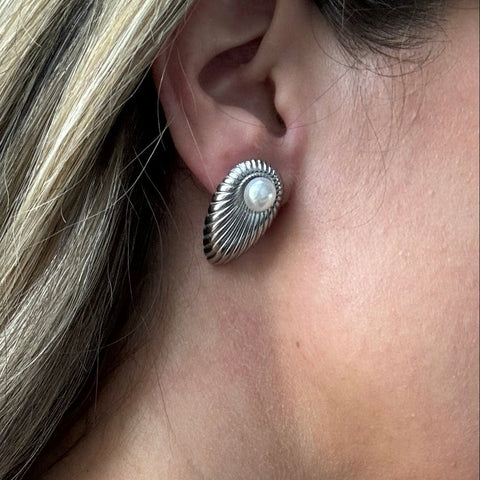 A close-up of a model's ear wearing a textured silver stud earring with a small white pearl at the center.